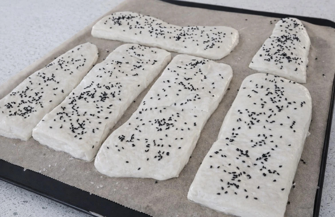 Bukë ciabatta të papjekura me fara të zeza mbi letër pjekjeje