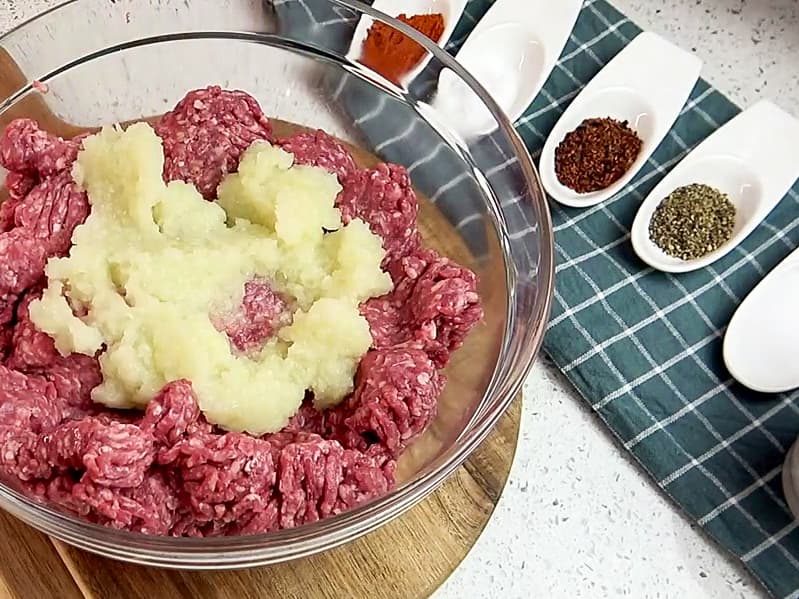 Përzierja e mishit të grirë me qepë, erëza dhe përbërësit e tjerë për qofte shtëpie.